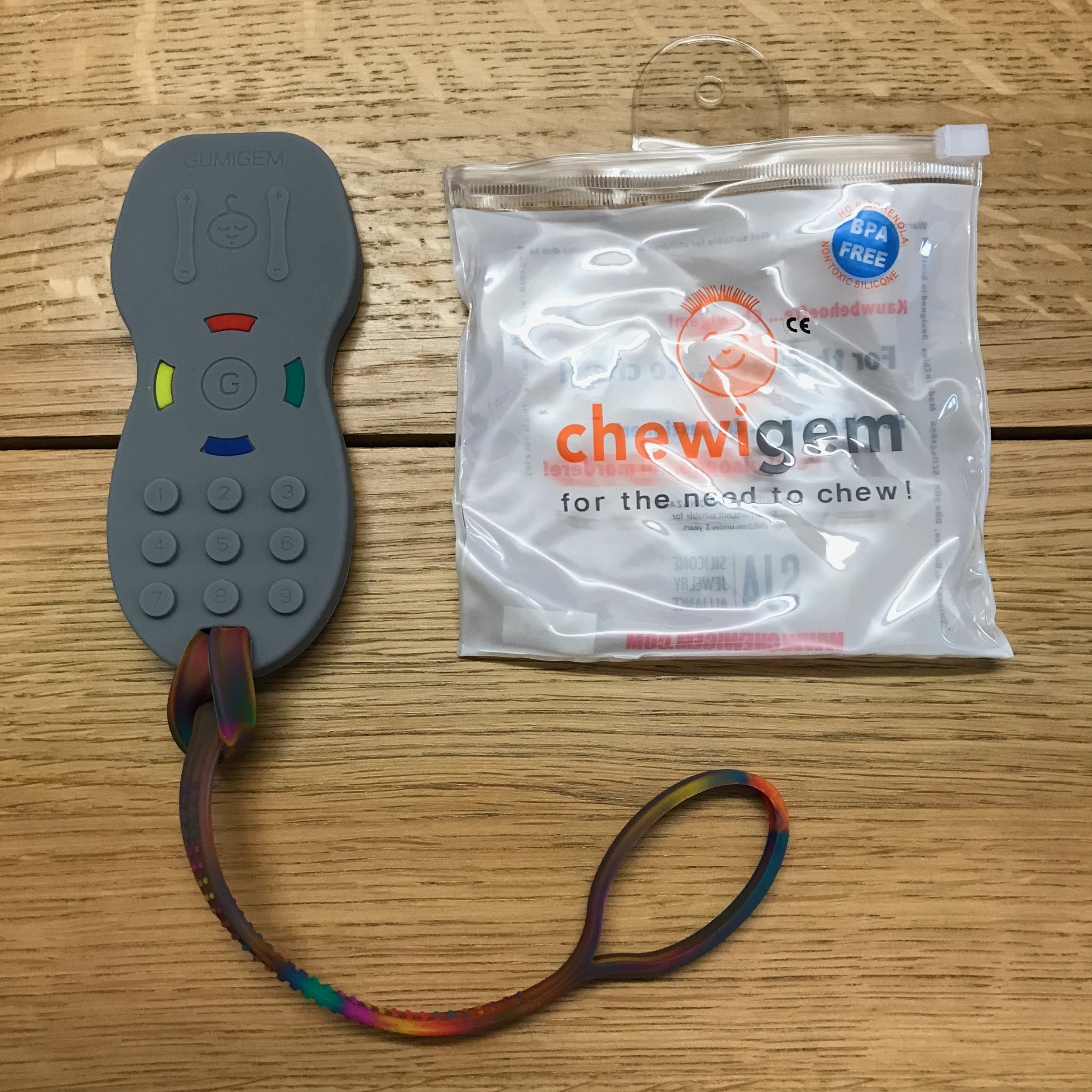 Photo of a chewigem chew toy in the shape of a TV remote, connected to a silicone strap
