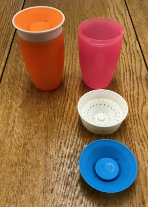 Photo of 2 munchkin 360 miracle cups. One connected together and the other showing the 3 components (beaker, screw top lid and valve)