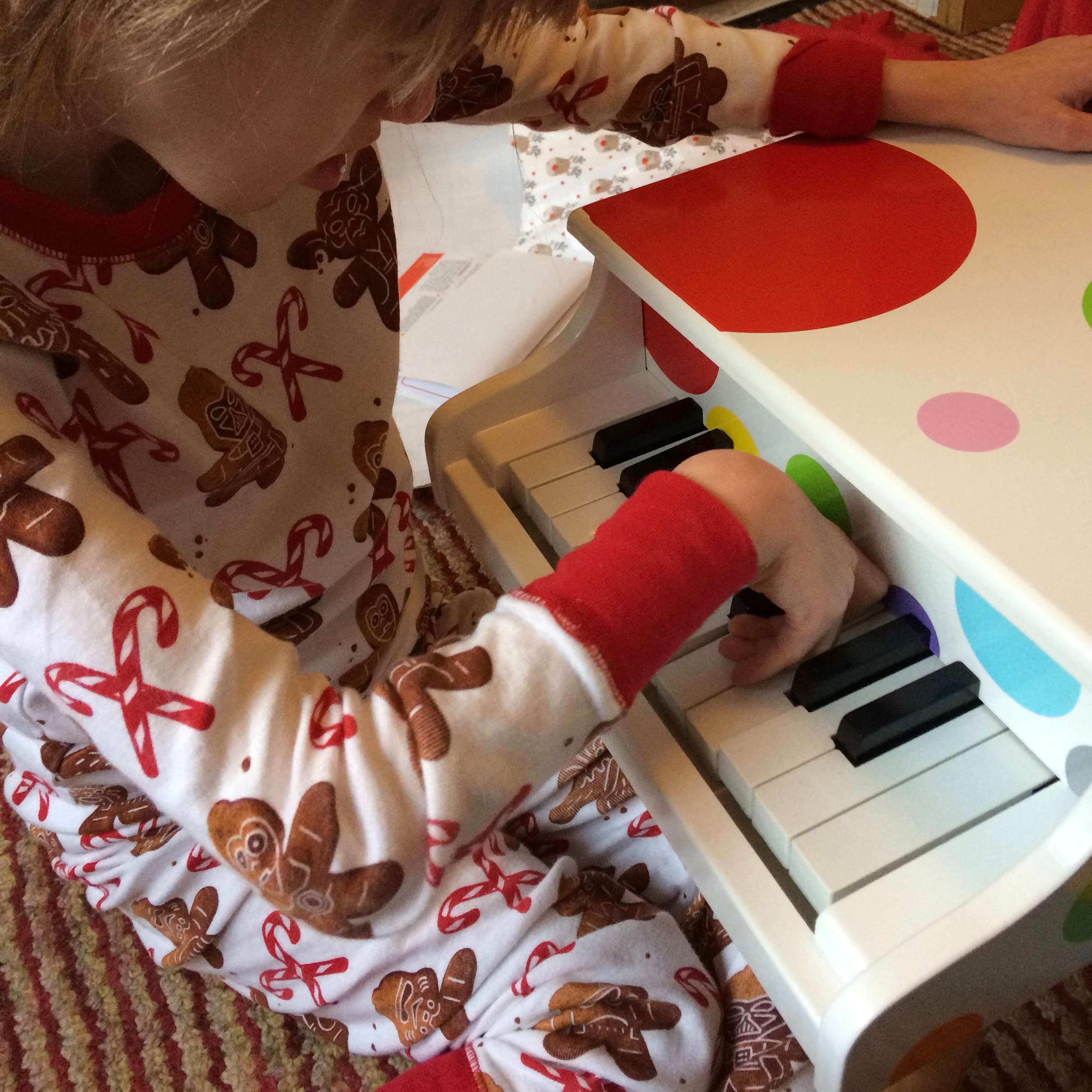 Close up of J in her christmas PJs, playing with a small wooden toy piano